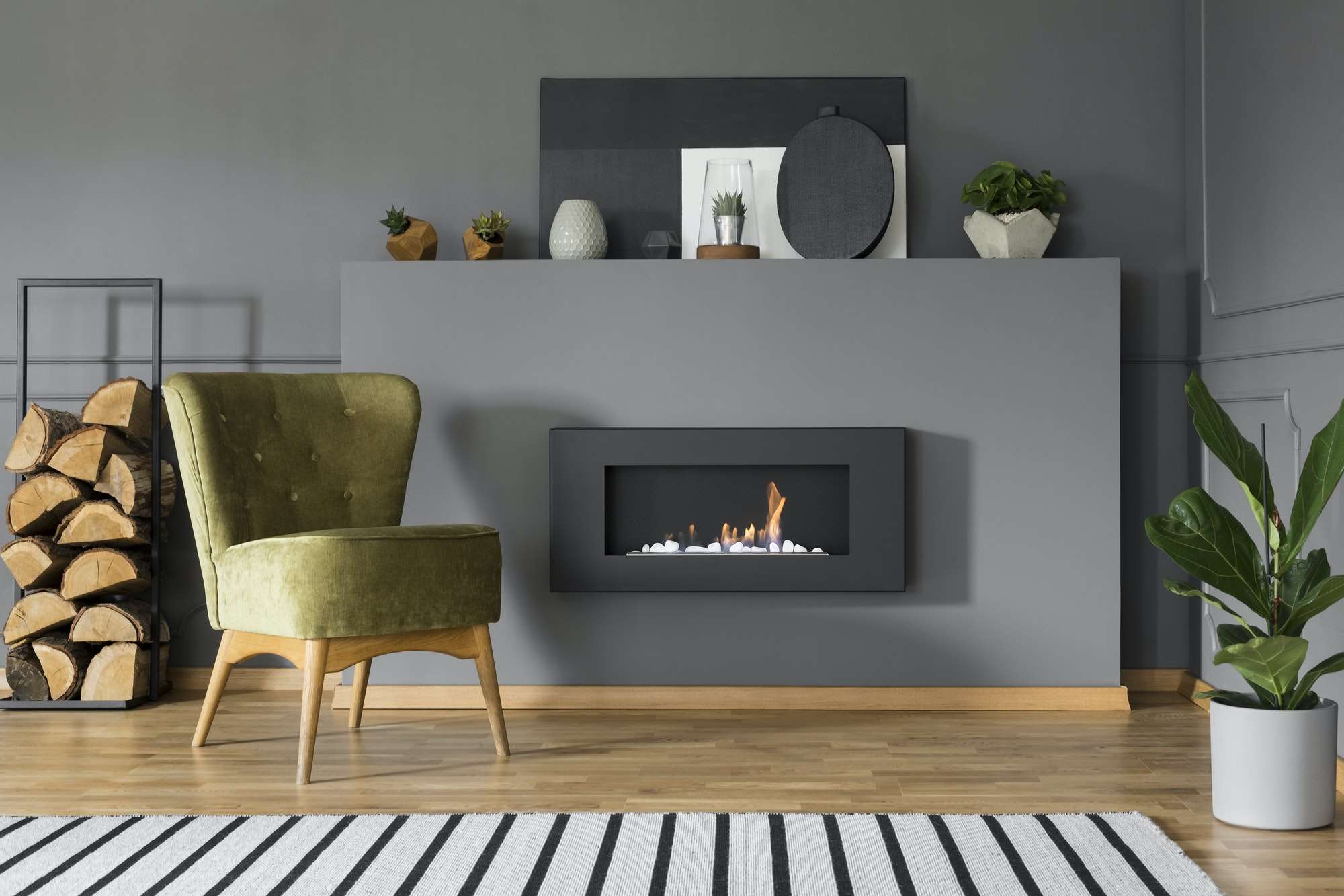 Green armchair and firewood next to fireplace in grey living roo