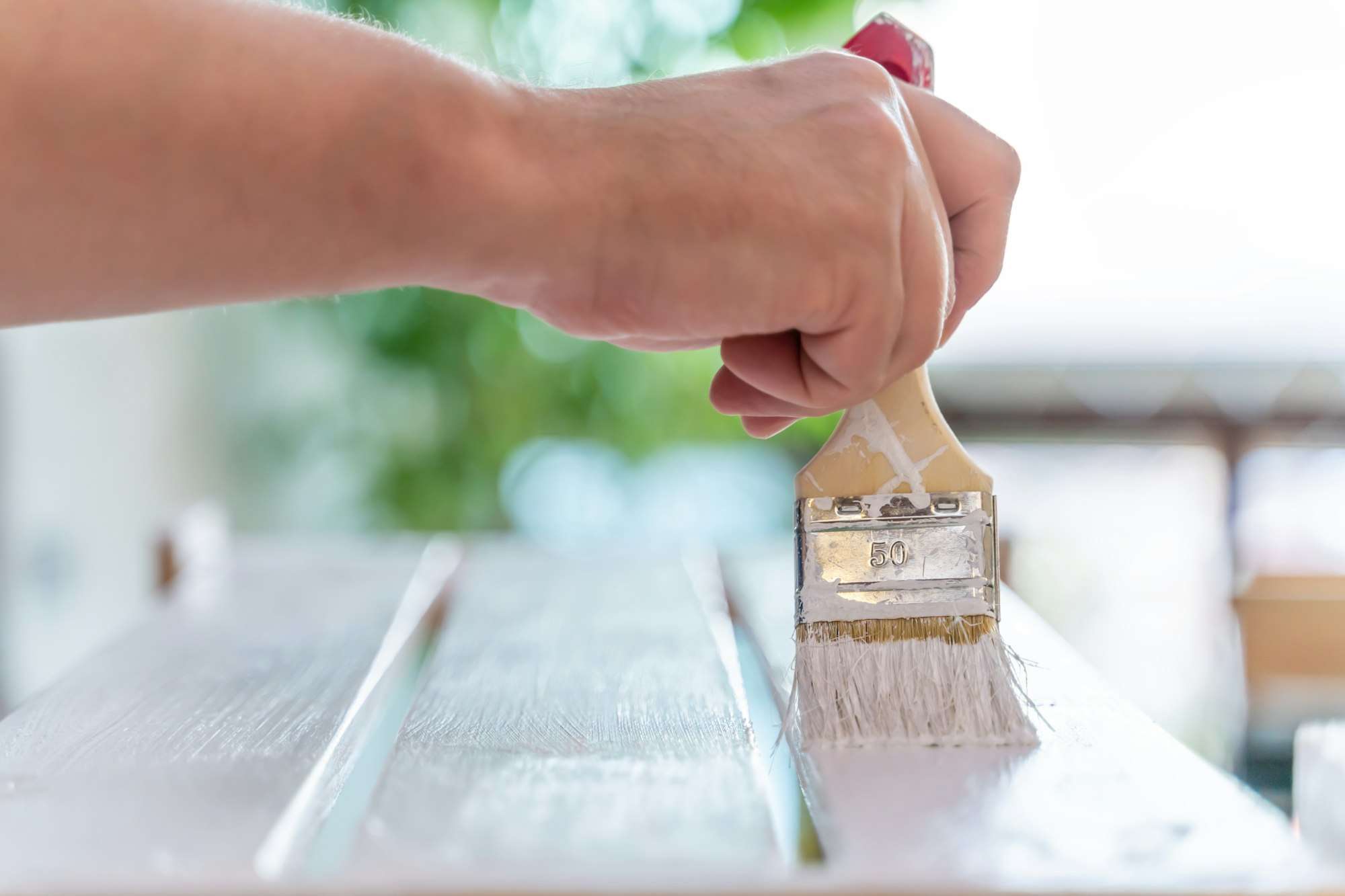 Man's hand paints wooden furniture with white paint with a brush closeup